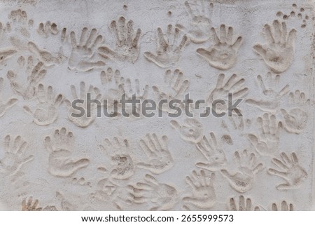 A textured wall features an array of handprints, creating a tactile and artistic display of human connection and creativity