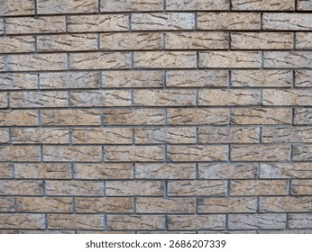 A textured wall made of rectangular beige bricks arranged in a uniform pattern. The surface shows subtle variations in color and texture.