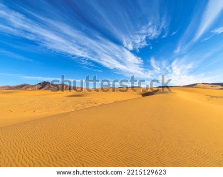 Textures sand ripples in foreground and a rocky mountain with a blue sky and stratus clouds with motion effect. Colorful smartphone photography in Tadrart Rouge, Djanet Algeria. Tassili N'Ajjer Sahara