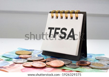 TFSA letters on notebook with coins and bills on a clear background