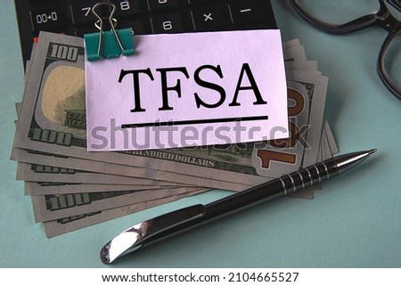 TFSA (Tax Free Savings Account) - acronym on a white piece of paper fixed on banknotes against the background of a calculator, glasses and pen. Business and finance concept