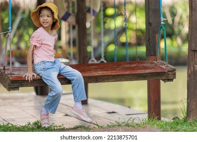 Thai Asian Kid Girl,age 5 To 7 Years Old, Looks Cute And Smiles Brightly, Dressed In Fashion Style.She Was Happily Sitting On The Swing On Vacation. Play Is Creative Learning Outside Of The Classroom.