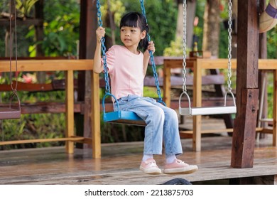 Thai Asian Kid Girl,age 5 To 7 Years Old, Looks Cute And Smiles Brightly, Dressed In Fashion Style.She Was Happily Sitting On The Swing On Vacation. Play Is Creative Learning Outside Of The Classroom.