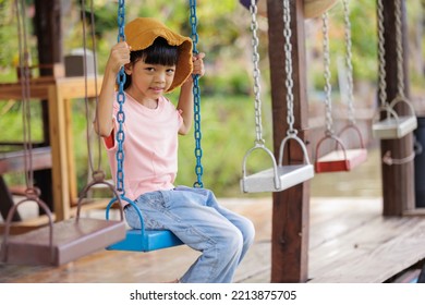 Thai Asian Kid Girl,age 5 To 7 Years Old, Looks Cute And Smiles Brightly, Dressed In Fashion Style.She Was Happily Sitting On The Swing On Vacation. Play Is Creative Learning Outside Of The Classroom.