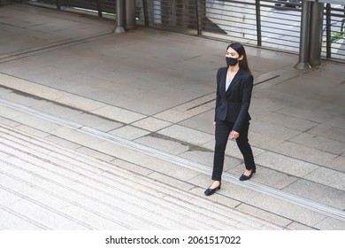 A Thai Asian Woman Wearing A Black Suit, Trousers And A Mask. She Was Walking Up The Stairs. In The Concept Of Travel And Advancement Of A Business Woman Or Office Worker.