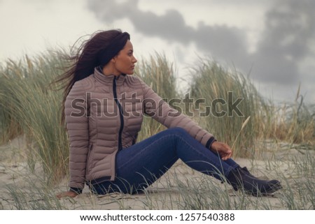 Thai (brazilian) woman holding a reed while sitting at the beach at windy weather.