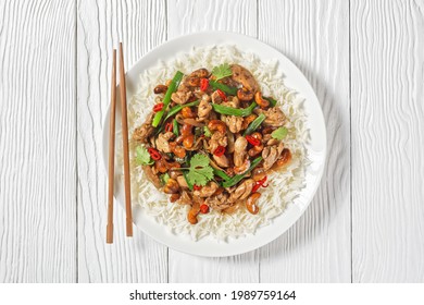 Thai cashew chicken stir fry served with a jasmine rice on a white plate on a wooden table with chopsticks, horizontal view from above, close-up - Powered by Shutterstock