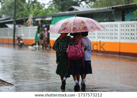 Thai children sharing umbrella in rain storm - blurred