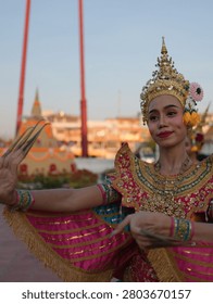 A Thai dancer performs graceful movements in an ornate pink costume near the Giant Swing.