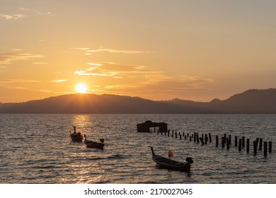 Thai fishing boats, a broken boat pier and the sea with a Thai island and golden sunset background