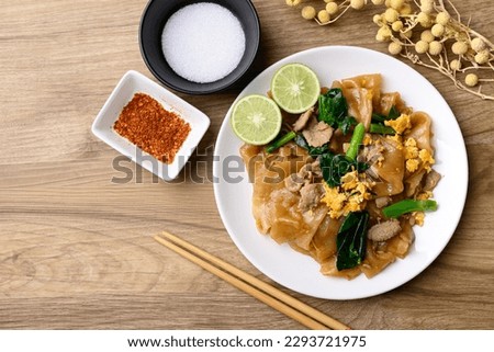 Thai food (Pad See Ew), Stir fried rice noodles soy sauce with pork, egg and kale on wooden background, Table top view