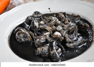 Thai food, Squid in black ink sauce - The best Thai seafood dishes in Bangkok Thailand,  with squid ink, pepper, garlic, lemon in a white plate on a wood background. Top view, close up
