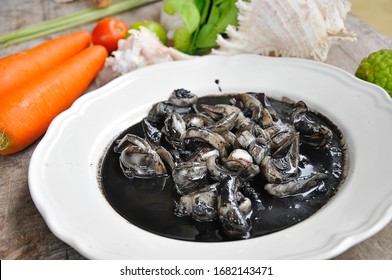 Thai food, Squid in black ink sauce - The best Thai seafood dishes in Bangkok Thailand,  with squid ink, pepper, garlic, lemon in a white plate on a wood background. Top view.