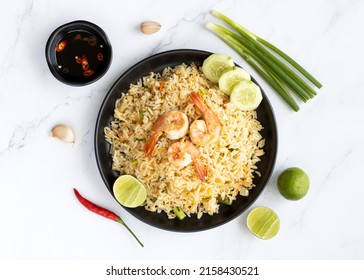 Thai Fried Rice With Shrimp, Green Onions, Lime, Garlic, Chili Peppers And Sauce In A Black Plate On A Marble Background, Top View.