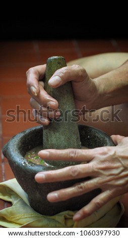 Thai woman’s hands hold stone granite pestle with shrimp paste chilli sauce in granite mortar.Thai food concept.