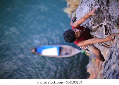 Thai Male Rock Climber Climbing Mountain Multi Pitch Route At Ao Nang Tower, Railay, Tonsai Beach With Blue Water Long Tail Boat On The Background, Krabi In Thailand, 