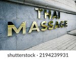 Thai massage inscription with golden letters on building facade outside. Massage parlor.