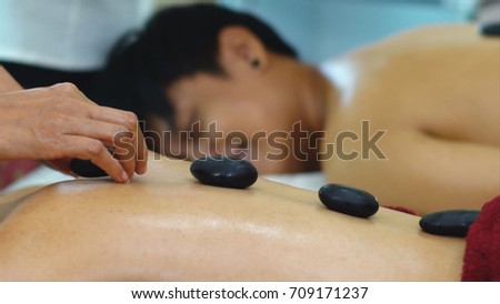 Thai masseur massage place the Hot stone on back woman is a natural therapy in which warmed stones are positioned on parts of the client's body of to relax tense muscles, relieve pain

