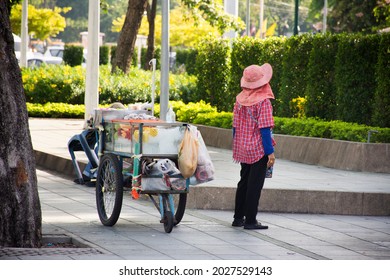 Thai old woman people push tricycle cart hawker on road sale variety fruits and food to siam people and foreign travelers eat and drink on pavement of Sanam Luang area at BKK city in Bangkok, Thailand