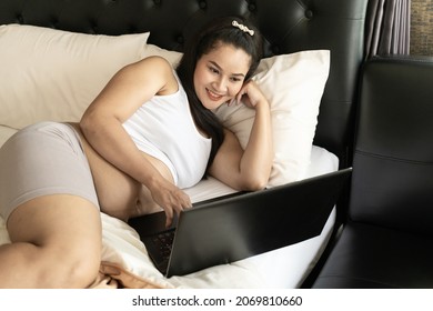 Thai Pregnant Mother Use A Computer For Online Shopping. She Choose To Buy Baby Clothes For The First Born On The Bedroom. She Smile And  Very Happy.The Idea Of Buying Baby Supplies.
