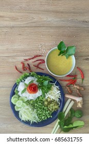 Thai Rice Noodle Eaten With Curry And Veg. Thai Food (Thai Language Kanom Jeen) On Blue Dish And Green Bowl, All On Brown Wooden Background / Flat Lay Style

