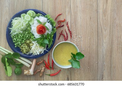 Thai Rice Noodle Eaten With Curry And Veg. Thai Food (Thai Language Kanom Jeen) On Blue Dish And Green Bowl, All On Brown Wooden Background / Flat Lay Style, And Space For Text

