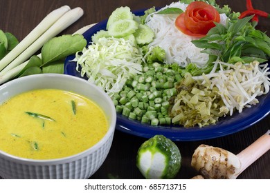 Thai Rice Noodle Eaten With Curry And Veg. Thai Food (Thai Language Kanom Jeen) On Blue Dish And Green Bowl, All On Brown Wooden Background / Selective Focus

