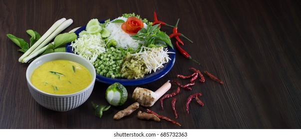 Thai Rice Noodle Eaten With Curry And Veg. Thai Food (Thai Language Kanom Jeen) On Blue Dish And Green Bowl, All On Brown Wooden Background / Selective Focus And Adjustment For Cover, Banner, Header

