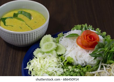 Thai Rice Noodle Eaten With Curry And Veg. Thai Food (Thai Language Ka Nom Jeen) On Blue Dish And Green Bowl, All On Brown Wooden Background / Selective Focus

