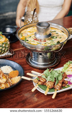 Thai spicy squid soup in metal pot and various seafood snacks on dinner table in cafe