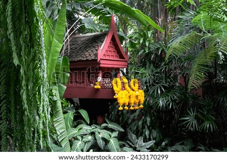 Thai spirit house worship ghost small wooden shrine wat yellow flower garland Hinduism Asia tropical garden decoration religion guardian