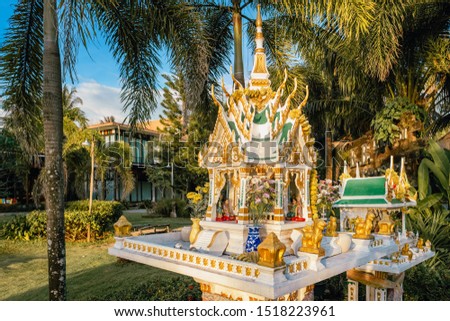 Thai spirit house yellow white colors with palms at background in Thailand