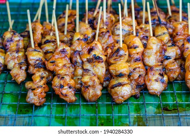 Thai street vendor sells grilled chicken meat at street food market in island Koh Phangan, Thailand. Close up fried chicken butts