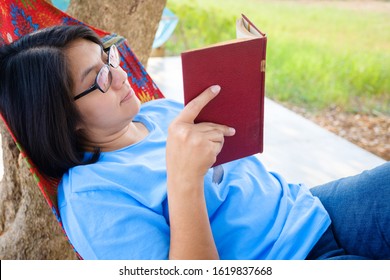 Thai woman in casual cloths read the book on the hammock at the backyard with green field on background