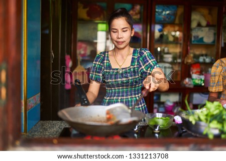 thai woman cooking red curry in wok inside traditional kitchen