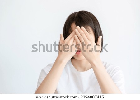 Thai woman covers her face with her own hands on a white background.