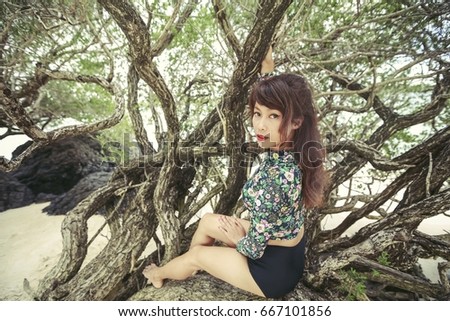 Thai woman wearing swimsuit long sleeves, she is sitting on tree's branches
