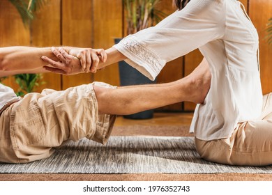 Thai yoga traditional therapeutic massage. Young female receiving full body massage by male therapist in standard Thai passive stretching position