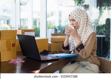 Thai Young Muslim Business Woman Wearing Hijab Sitting At Table Work Place Drinking Water. Stay Hydrated.