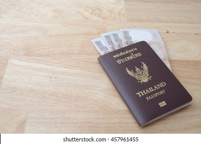 Thailand passport and Thai money on wooden table (Thai language on passport book is Thailand Passport), blurred - Shutterstock ID 457961455