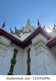 A Thai-style church with the serpent king of nagas in each corner of the church, a blue sky background, and sunlight in the upper right corner of the church.