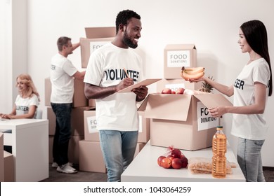 Thank you. Beautiful brunette standing in semi position and holding bananas while looking at her colleague
