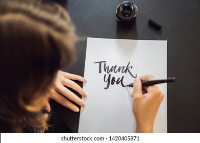 Thank you. Calligrapher Young Woman writes phrase on white paper. Inscribing ornamental decorated letters. Calligraphy, graphic design, lettering, handwriting, creation concept