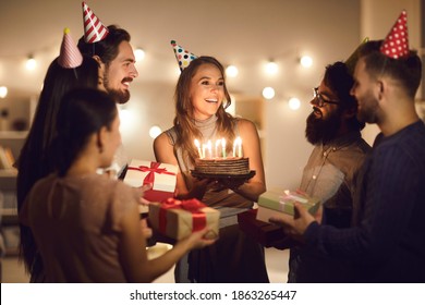 Thank You, Guys. A Happy Young Woman In Her Twenties Holding Her Birthday Cake With Burning Candles And Thanking Her Friends For Such A Great Surprise And All The Presents During A Party At Home