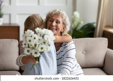 Thank you, my dear! Excited aged grandmother or mature female babysitter feeling grateful and happy embracing with warmth little girl ward or granddaughter giving her flowers congratulating on holiday