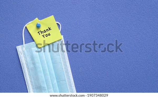 Thank you note on top of medical face mask. Pin on\
blue board. Copy space.
