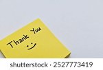 Thank you with smile icon on yellow sticky note, isolated on a grey background.