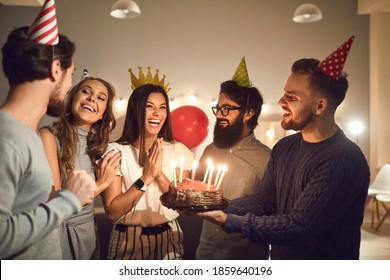 Thank you for the surprise, guys! Bunch of friends giving delicious, sweet birthday cake with lit candles to happy, laughing, young woman in her twenties during party at home, in cafe or restaurant - Powered by Shutterstock