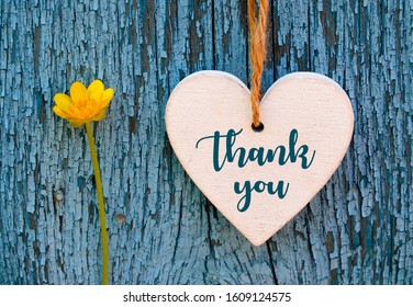 Thank You or thanks greeting card with yellow flower and decorative white heart on blue wooden background.International Thank You Day concept.Selective focus.