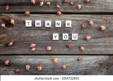 Thank you word is made of bright wood cubes with black letters and small pink roses  on a dark wooden background